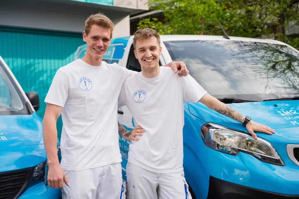 Zwei Männer in weißen T-Shirts vor Lieferwagen.
