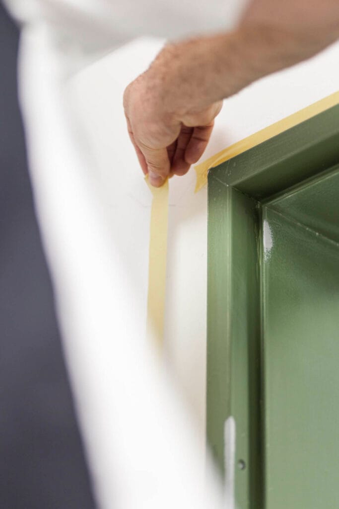 Hand klebt Malerkrepp an Türrahmen